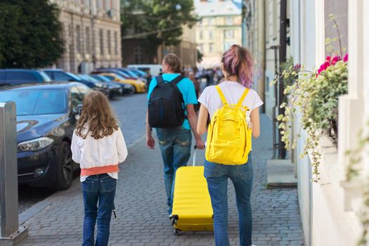 Children two girls daughters and father, tourists walking around city with backpacks and a suitcase. Travel, family, vacation, tourism, summer concept