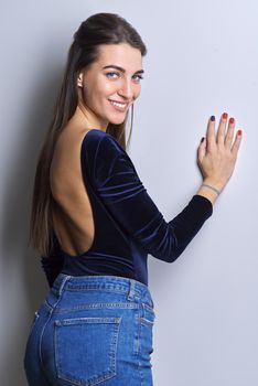 Portrait of young woman looking at camera on white background. Beautiful smiling female with healthy white toothed smile, straight long hair in blue fashionable clothes, jeans