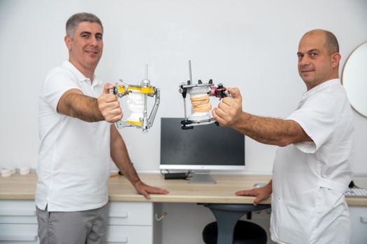 Two male dentists holding dental articulators in a dental clinic