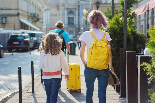 Children two girls daughters and father, tourists walking around city with backpacks and a suitcase. Travel, family, vacation, tourism, summer concept