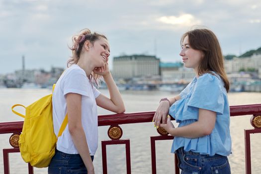 Portrait of two teenage girls friends walking and talking on pedestrian bridge on sunny summer day. Friendship, lifestyle, youth, teens