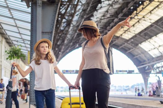 Happy mother and daughter child walking together at railway station with luggage suitcase. Travel, tourism, transportation, family concept