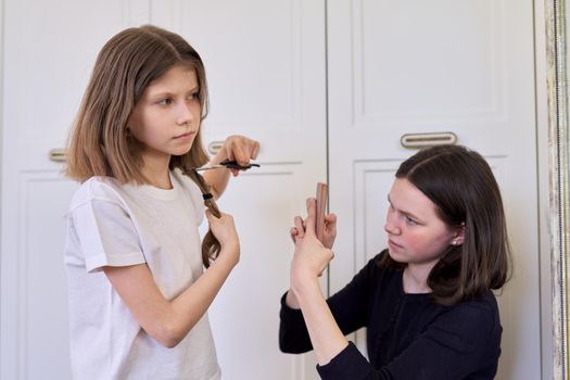 Girl child cuts her own hair with scissors, older sister teenager makes videos on smartphone, for social networks, blog, channel