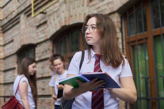 Girl teenager college student posing outdoor in white T-shirt with tie in glasses. Background brick building, group of girls students. Beginning of classes, back to college, copy space