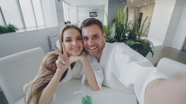 Point of view shot of attractive loving couple recording video while relaxing in day spa together. Happy young people are smiling, laughing and kissing looking at camera.