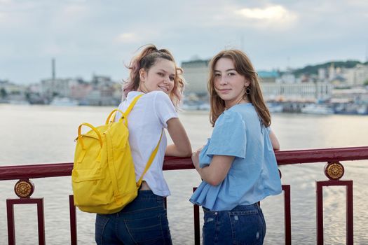 Portrait of two teenage girls standing on bridge over river, friends walk on summer sunny day. Friendship, lifestyle, youth, teens