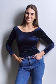 Portrait of young woman looking at camera on white background. Beautiful smiling female with healthy white toothed smile, straight long hair in blue fashionable clothes, jeans