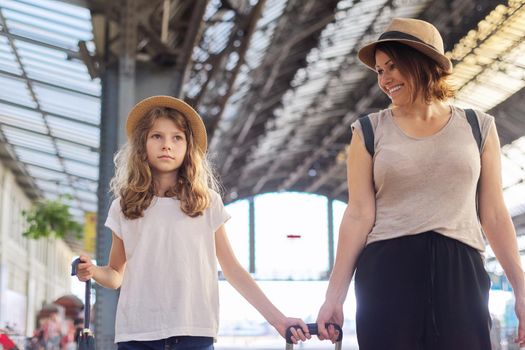 Happy mother and daughter child walking together at railway station with luggage suitcase. Travel, tourism, transportation, family concept