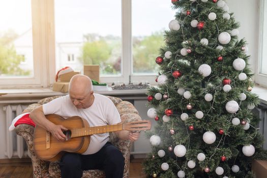 Happy people family concept - Old senior man enjoying the guitar on the sofa in the house at christmas.