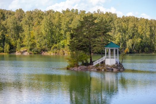 A small beautiful island on Lake Aya in the Altai Territory or the Altai Republic. There is a small gazebo on the island and a forest around the lake.