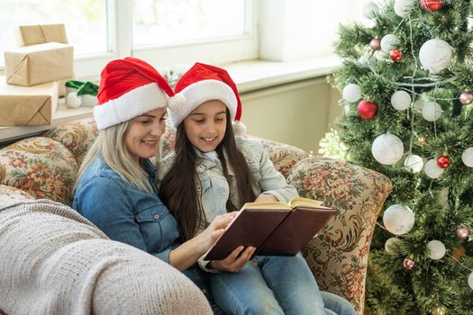 Mother with her child daughter celebrating near Christmas tree.