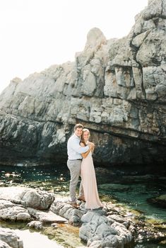 Man hugs woman standing on the rocks in the water near the cliff. High quality photo