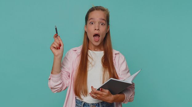 Thoughtful journalist teenager young girl making notes, writing down thoughts with pen into notepad notebook diary, to do list, good idea. Student child kid isolated on blue studio background indoors