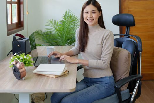 Portrait of a woman sitting at home working on a computer on her desk.