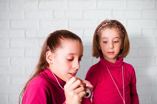 Couple of Little Girls Taking Picture Using Toy Photo Camera, white brick wall on background