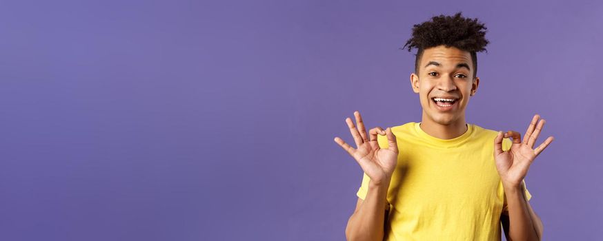 Close-up portrait of upbeat, relaxed young hipster guy with dreads assuring all good, everything be okay, show OK gesture and smiling, no problem guarantee best quality, purple background.