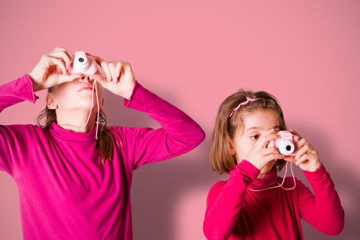 Couple of Little Girls Taking Picture Using Toy Photo Camera, pink wall on background