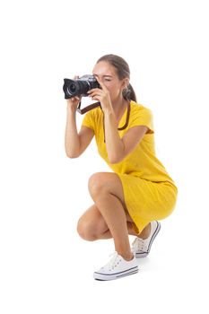 Young caucasian woman in yellow dress takes images with photo camera. Full length portrait. Isolated on the white background.
