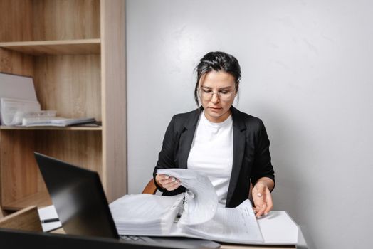 Image of a woman jotting down notes while sitting at a desk in an office. A girl working with papers in an office. Real office.