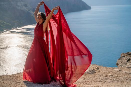 A woman in a red flying dress fluttering in the wind, against the backdrop of the sea