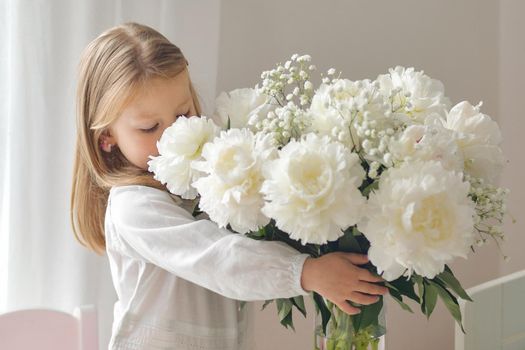 A little girl smelling a bouquet of the white peonies