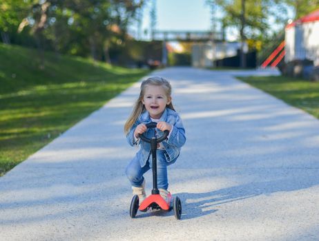 Little girl of 3 years old is riding a scooter