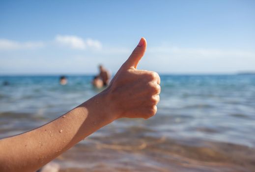 Female hand thumbs up on sea and sky background closeup. Woman showing ok sign on shoreline coastline. Body language, communication concept. Holiday, vacation, summer is coming conceptual photo.