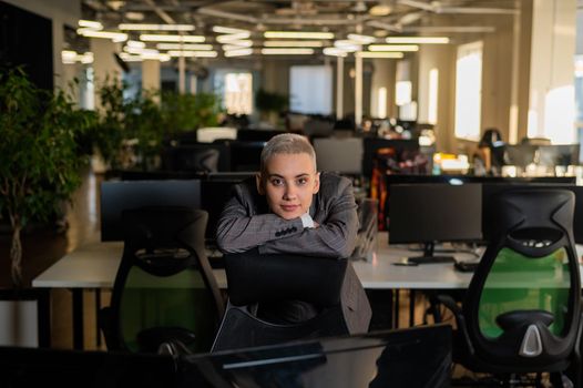 Pensive young woman with short hair sits in armchair in office