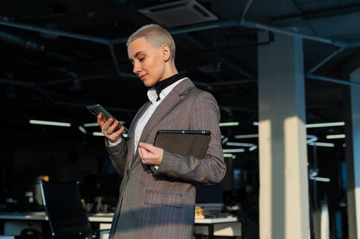 Pensive young woman with short hair uses mobile phone in office
