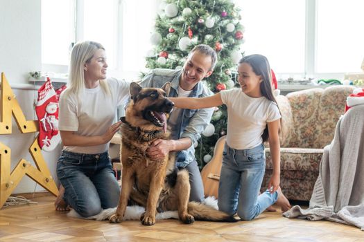 Merry Christmas and Happy New Year. Happy family with dog are waiting for the New Yearwhile sitting near beautiful Christmas tree at home