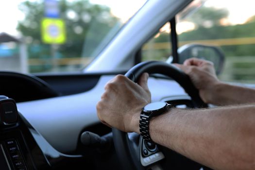 Beautiful male hands with a smart watch holding the steering wheel while driving a car. Safe driving concept.