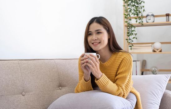 Young asian woman drinking coffee on a sofa bed at home.