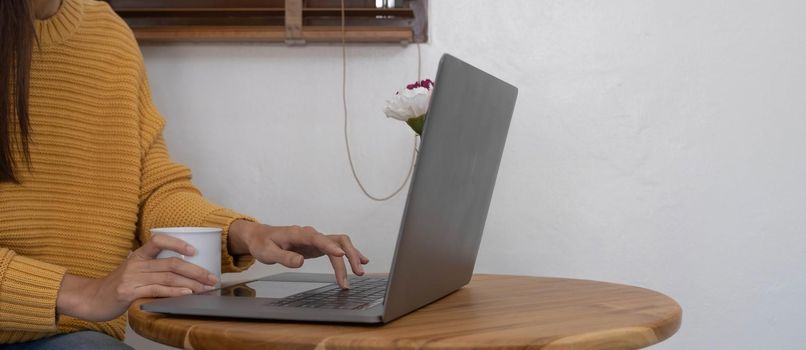 Beautiful young Asian woman holding a cup of hot black coffee on the table while working. Asian young woman enjoy drinking a hot coffee in the morning before starting online meeting from home..