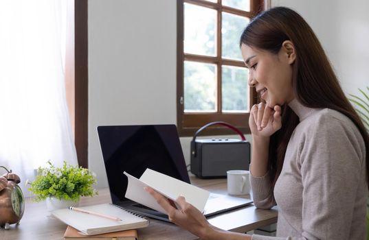 Attractive young woman sits in a chair and looks at a book in her hand. girl on the right There is a laptop on the desk in the office..