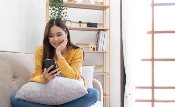 Free time. Asian girl checking social networks on phone, resting on sofa, panorama with free space.