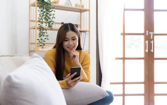 Free time. Asian girl checking social networks on phone, resting on sofa, panorama with free space.