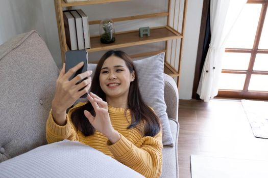 Young asian woman is using smartphone lie down on the sofa. Relax, happy, technology concept.