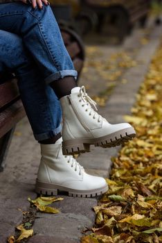 Female legs in a jeans and white fashion boots with laces. fallen leaves on the sidewalk