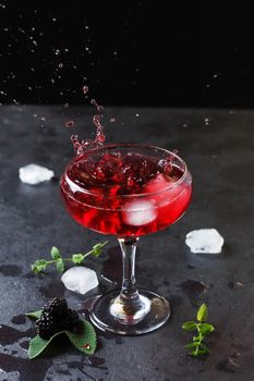 Splash of blackberry cocktail in a glass on a black background.