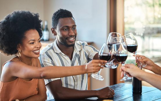 Black couple celebrating their anniversary with friends, toasting and drinking red wine. Happy girlfriend and boyfriend bonding at a family gathering, together for an engagement or proposal.