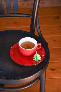 A red cup with tea is wrapped in a warm Christmas sweater, a tea bag label in the form of a green Christmas tree. High quality photo