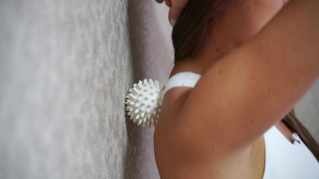 Athletic slim caucasian woman doing thigh self-massage with a massage ball indoors. Self-isolating massage.