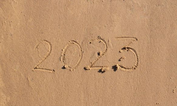 The numbers 2023 are written on the sand on the beach. The concept of the New Year. Happy New Year 2023 background. Travel during the Christmas holidays