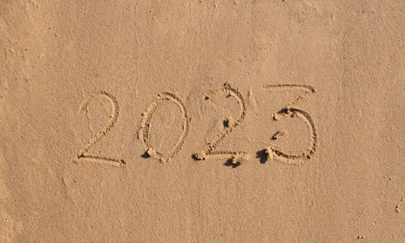 The numbers 2023 are written on the sand on the beach. The concept of the New Year. Happy New Year 2023 background. Travel during the Christmas holidays