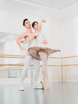 Training before performance. Man dancing classical ballet, he rotating pretty woman in white tutu dress in gym or ballet hall. Couple perform sensual dance. Minimalism interior.