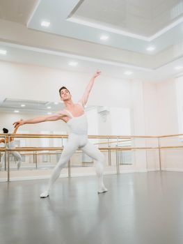 Young handsome male dancer practicing in classical ballet in small studio with mirrors. Man in white tights. Professional choreographer is working on creating performance.