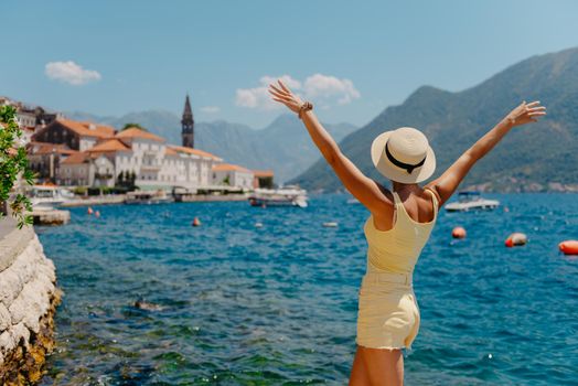 Summer photo shoot on the streets of Kotor, Montenegro. Beautiful girl in white dress and hat. smiling tourist girl with hat. Spectacular view of Montenegro with copy space. fashion outdoor photo of beautiful sensual woman with blond hair in elegant dress and straw hat and bag, posing in Montenego's city Perast