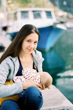 Mom breastfeeds her baby while sitting on the pier. High quality photo