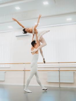 Training before performance. Man dancing classical ballet, he rotating pretty woman in white tutu dress in gym or ballet hall. Couple perform sensual dance. Minimalism interior.