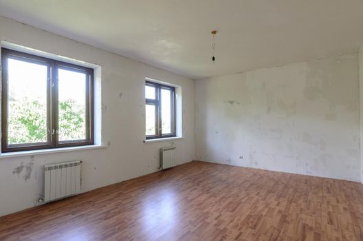 Interior of an empty room during renovation, there are two large windows in the room a